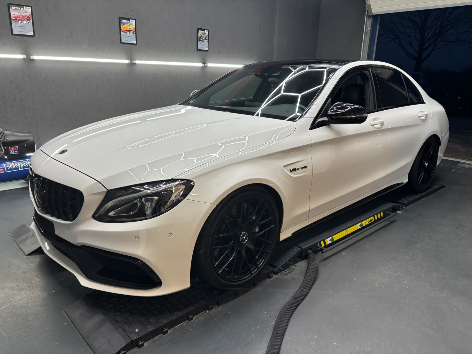 Weißer Mercedes-AMG C 63 in der Aufbereitungshalle, die Deckenleuchten spiegeln sich ungebrochen im Lack