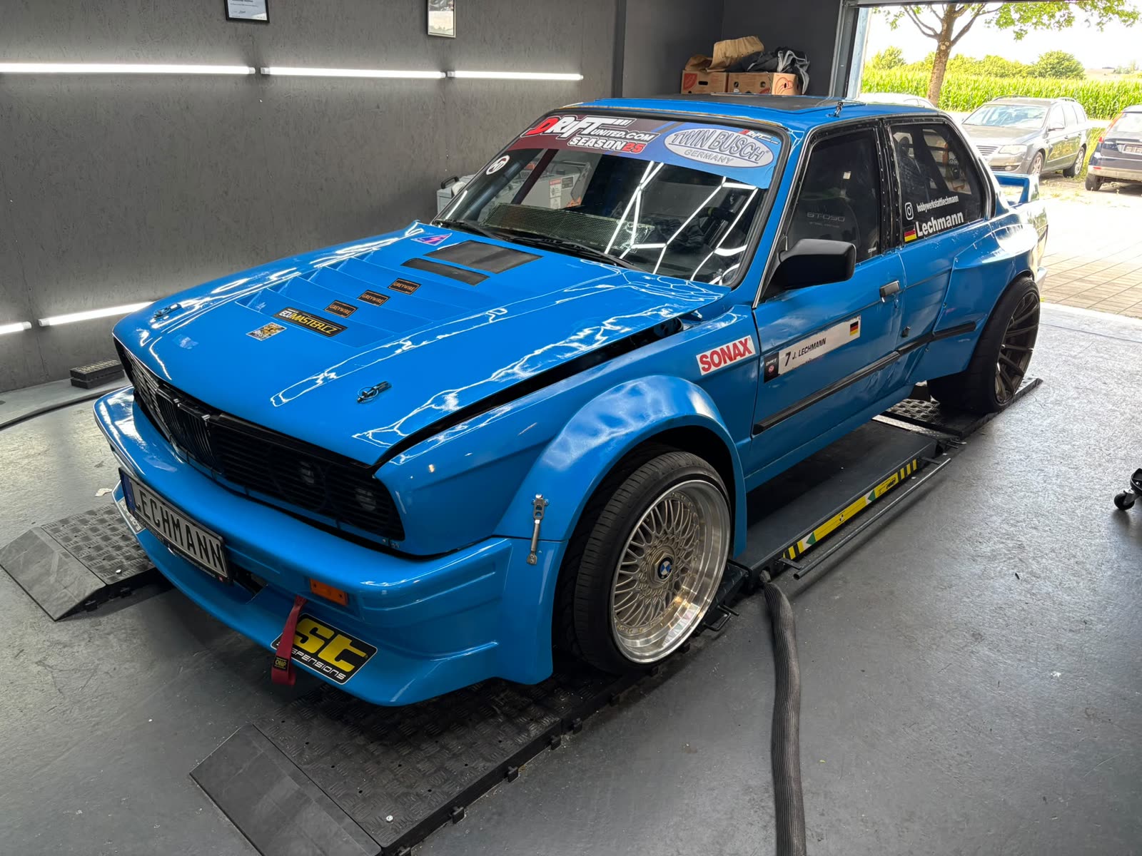 Hellblauer BMW E30 mit Breitbau und Überrollkäfig auf der Hebebühne in der Aufbereitungshalle