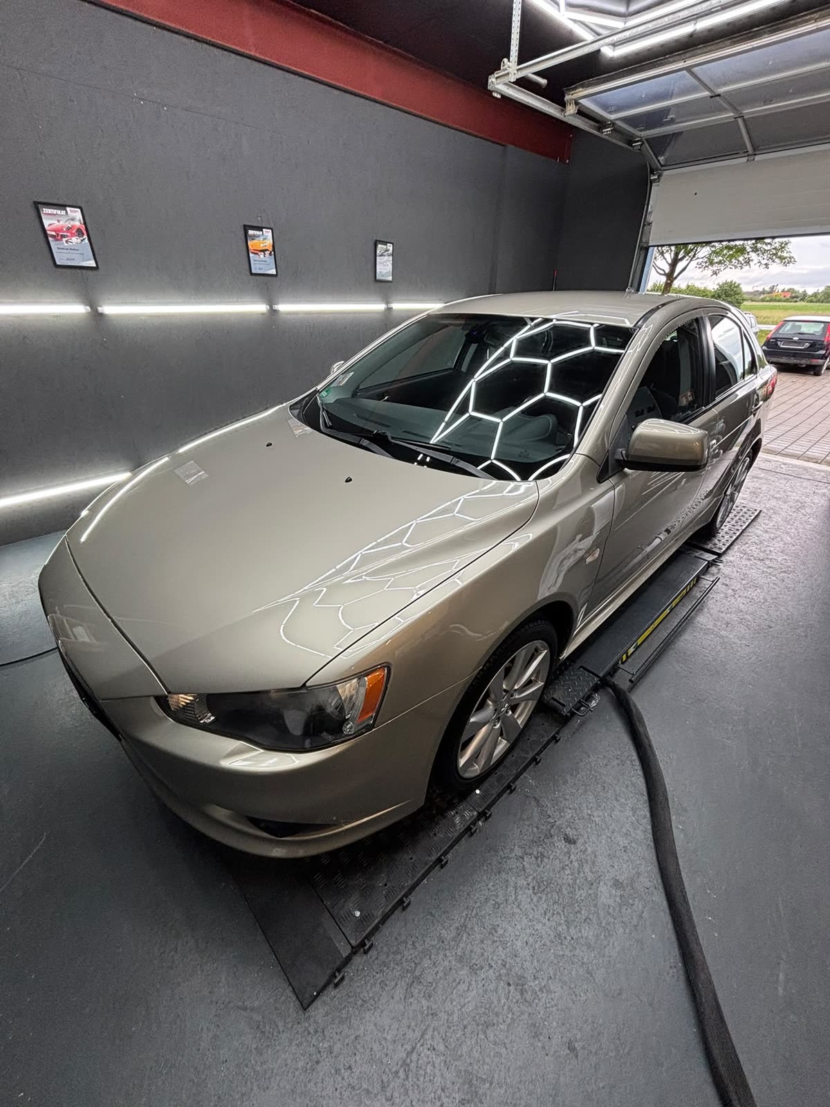 Beigefarbener Mitsubishi Lancer in der Aufbereitungshalle unter der Wabenbeleuchtung