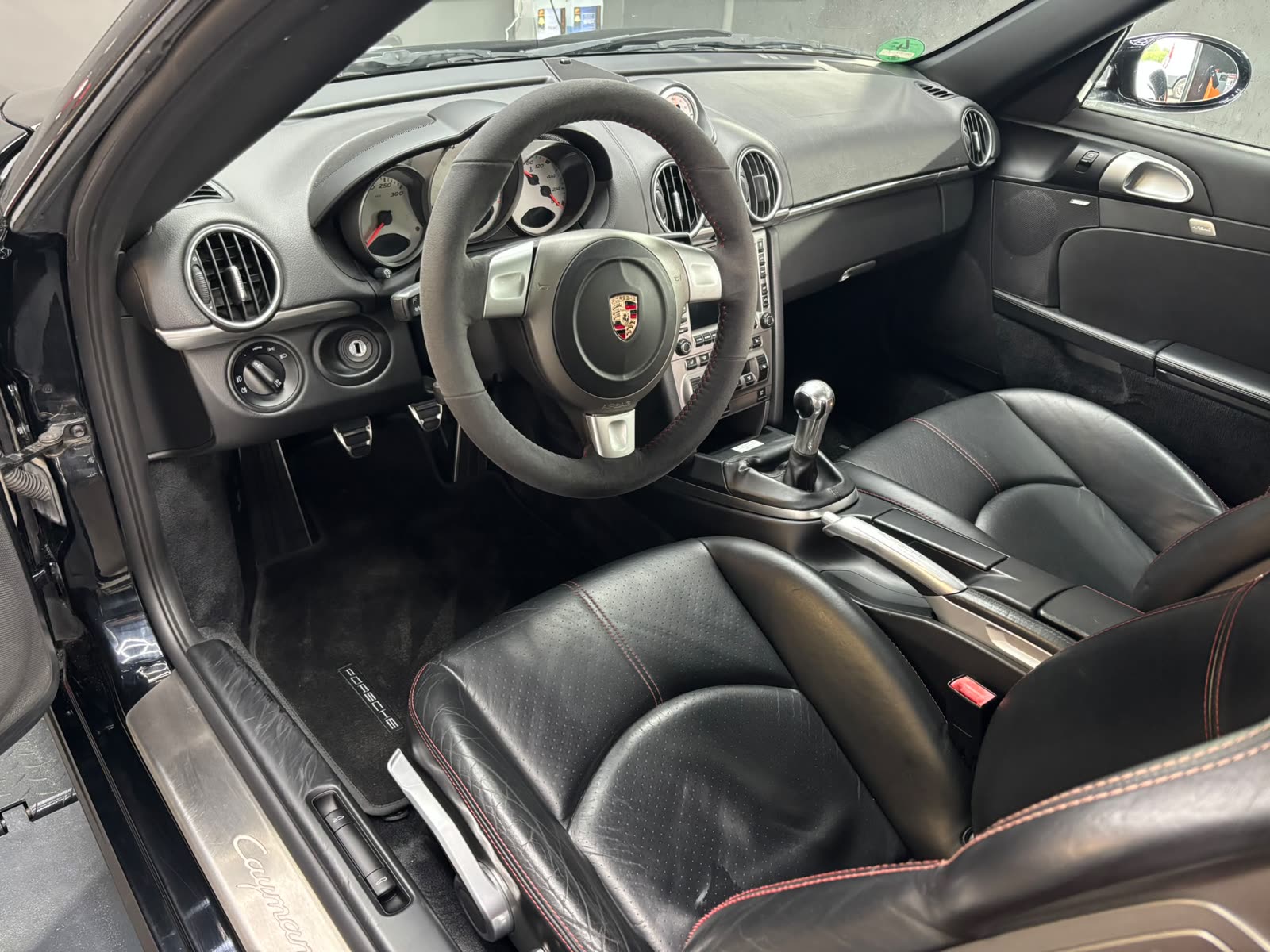 Innenraum eines Porsche Cayman S mit Alcantara-Lenkrad und schwarzen Ledersitzen mit roter Naht