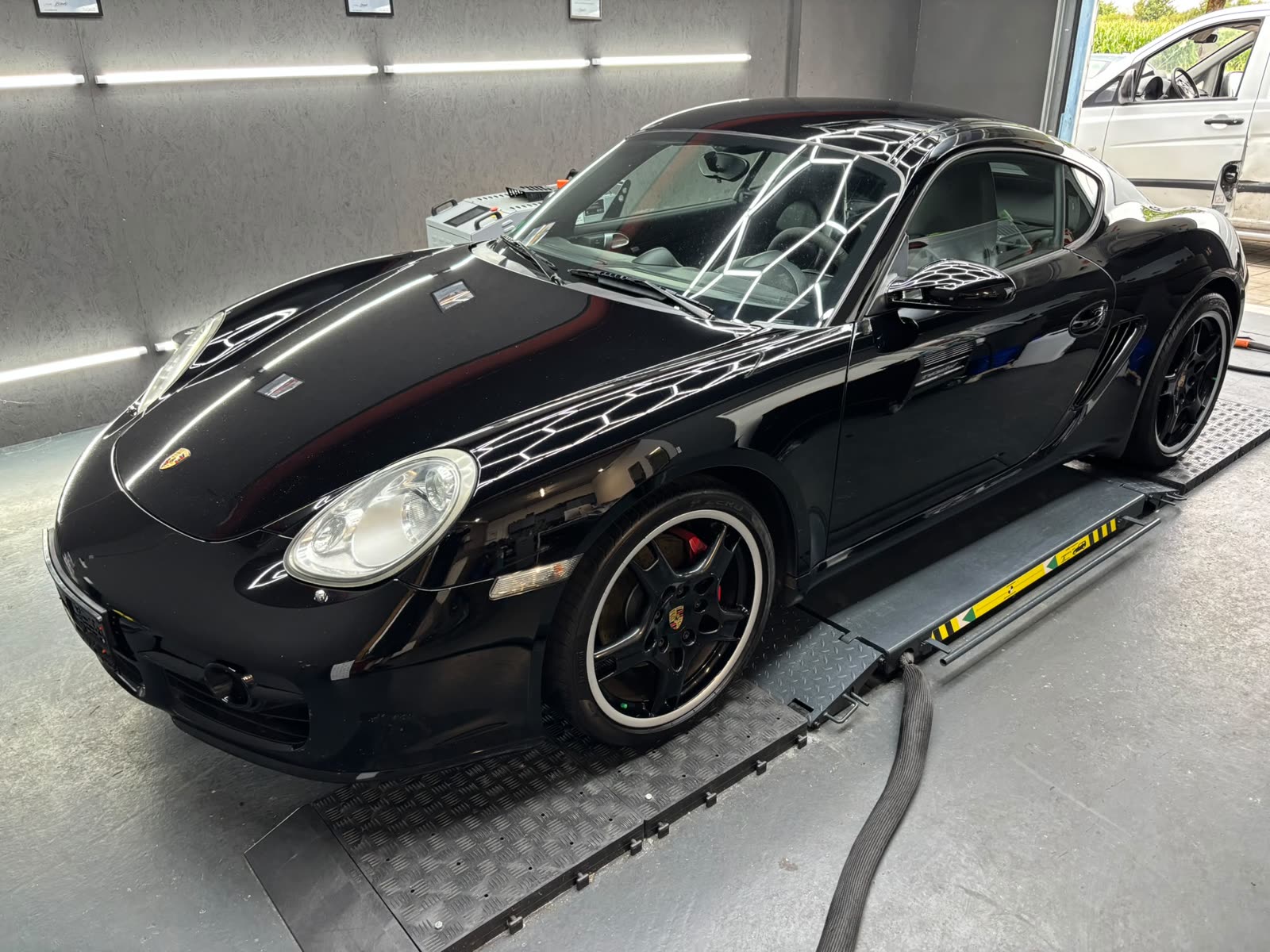 Schwarzer Porsche Cayman S in der Halle, der Lack spiegelt die wabenförmige Deckenbeleuchtung